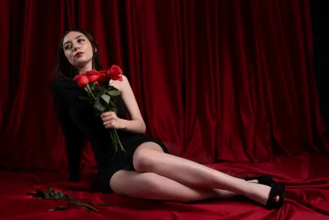 Elegant woman in a black dress holding red roses against a luxurious red velvet curtain background.
