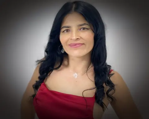 Smiling woman in a red dress and silver necklace posing against a soft grey studio background.
