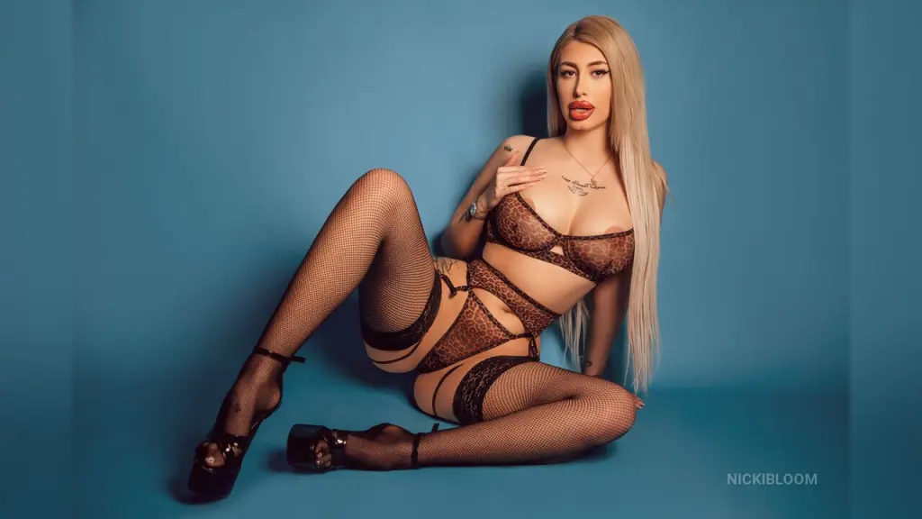 ViviAnne β NickiBloom poses in brown lace lingerie and fishnet stockings against a blue background.