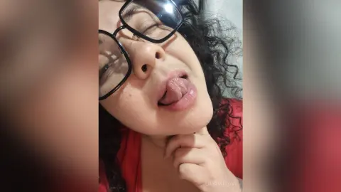 Young woman with curly hair and glasses making a playful expression in a casual indoor setting.