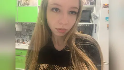 AdenaMcfalls with long blonde hair wearing a black top, looking directly at the camera in a kitchen setting.