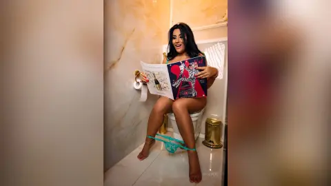 MissyJolie sits on a toilet wearing blue lace lingerie while holding an open magazine in a marble bathroom.