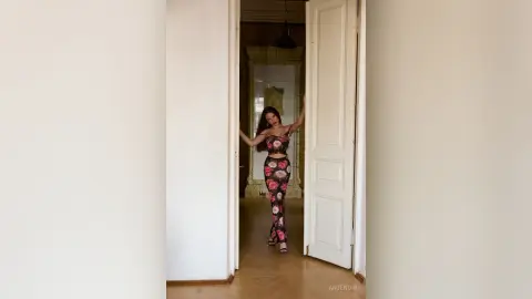 AnjeNoir poses in a floral crop top and matching tight leggings while standing in a doorway.