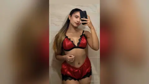 Young woman in red satin lace lingerie taking a mirror selfie in a modern bathroom.