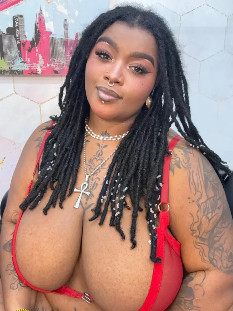 LaylaCumninngss poses with glasses and silver necklaces, showing off her large floral tattoos and nose ring.