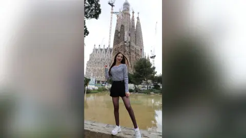 Young woman in a striped shirt and black skirt posing in front of the Sagrada Familia in Barcelona.