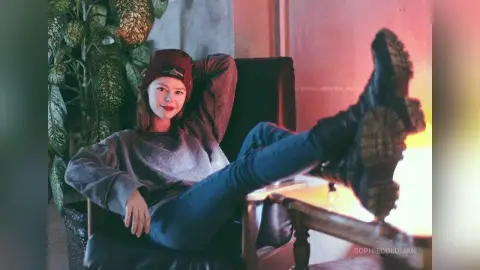 Relaxed woman in a grey sweatshirt and jeans lounging in a cozy, dimly lit room.