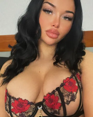 Beautiful woman with long dark hair wearing a red floral lace lingerie set in a soft indoor setting.