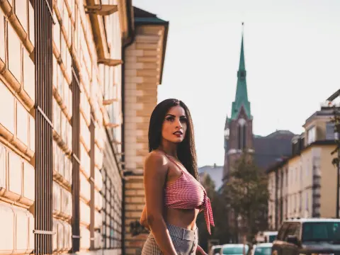 Stylish woman in a red gingham crop top standing on a sunny urban street near historic European architecture.