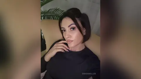 Young woman in a black long-sleeve shirt relaxing indoors with a moody, soft-lit aesthetic.