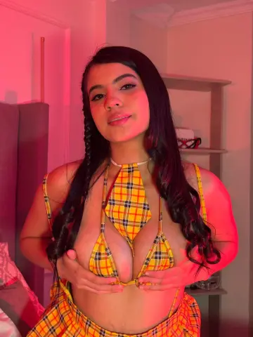 Young woman in yellow plaid bikini top posing in warm pink lighting indoors.
