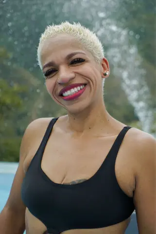Smiling woman with short blonde hair in a black sports bra enjoying a sunny day outdoors.