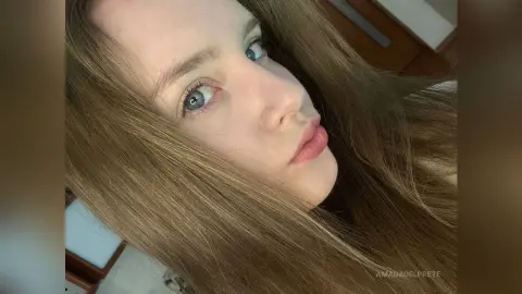 Close-up portrait of a young woman with long brown hair and blue eyes looking into the camera with a soft expression.