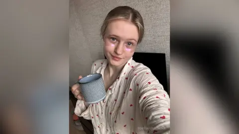 Young woman in white patterned pajamas holding a blue mug in a cozy indoor setting.