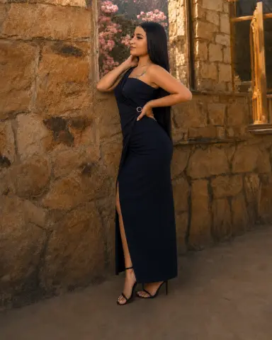 Elegant woman in a navy blue evening gown leaning against a rustic stone wall during golden hour.