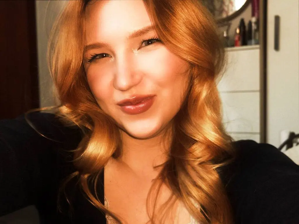 Smiling woman with wavy strawberry blonde hair wearing a black top in warm indoor lighting.