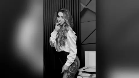 Smiling young woman in a white button-down shirt posing in a modern black and white interior setting.