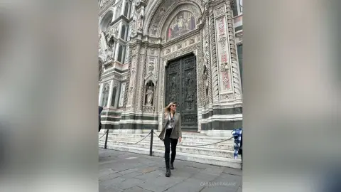 Stylish woman in a grey blazer and black trousers walking past the ornate Florence Cathedral architecture.