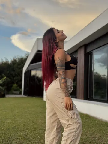 Tattooed woman in black crop top and beige cargo pants posing outdoors in soft sunset lighting.