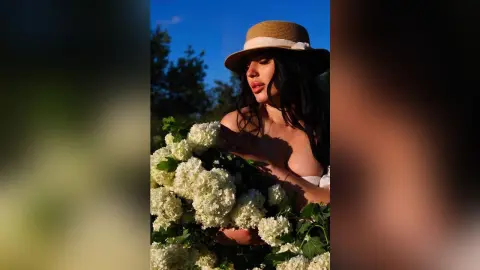 Beautiful woman in a straw hat holding white hydrangeas in a sunlit garden during golden hour.