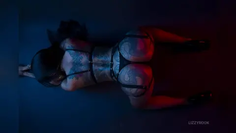 Tattooed woman in black lace lingerie lying on a dark blue floor with moody red lighting.