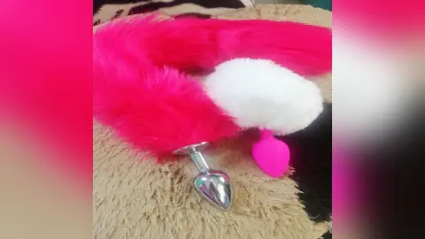 Pink and white faux fur plug with a silver metal base resting on a soft shag rug.
