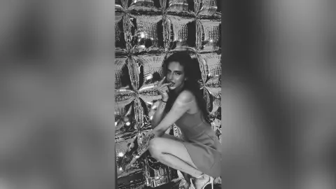 Glamorous woman in a sleek dress posing against a shimmering silver foil backdrop in a moody black and white photo.