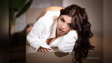 Beautiful woman in a white oversized shirt lounging in a modern indoor setting with a soft, moody aesthetic.