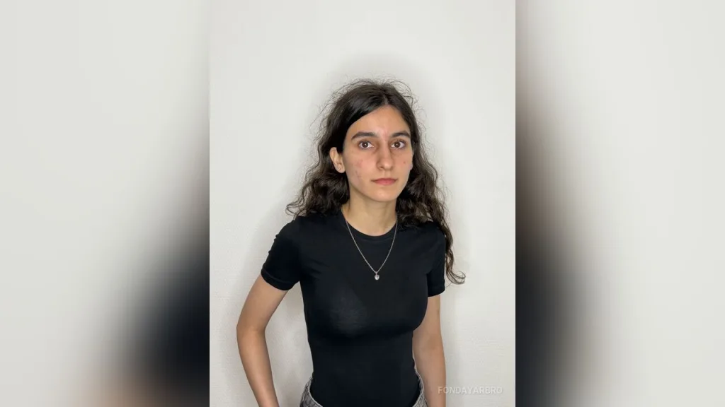 FondaYarbro — FondaYarbro wears a tight black t-shirt and stands against a white wall.