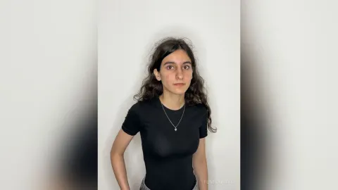 FondaYarbro — FondaYarbro wears a tight black t-shirt and stands against a white wall.