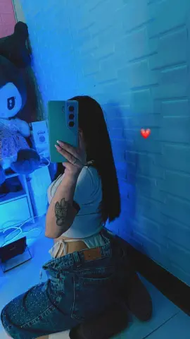 Young woman in white crop top and denim jeans taking a mirror selfie in blue moody lighting.