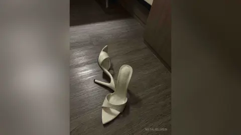 Elegant white high heel stiletto sandals on a dark wood floor in a modern indoor setting.