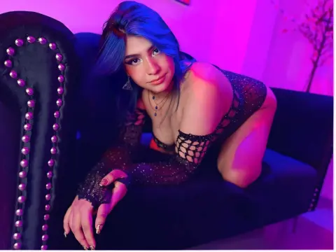 Woman with blue hair in a black sheer lace outfit lounging on a velvet sofa under moody purple neon lighting.