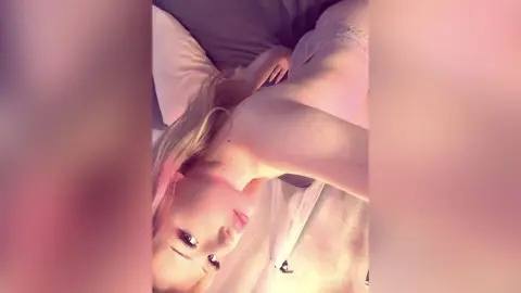 Blonde woman in white lace lingerie relaxing on a bed in soft, warm lighting.