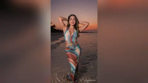 LilianMendoza poses on a beach at sunset wearing a tight, low-cut patterned sundress with her hands behind her head.