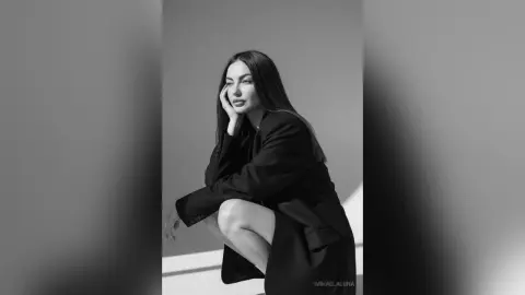 Elegant woman in a black blazer posing against a minimalist grey background in a moody black and white portrait.