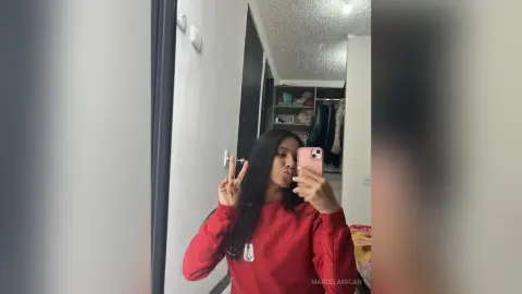 MarcelaMilan takes a mirror selfie wearing a red long-sleeve shirt and flashing a peace sign.