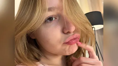 Blonde woman with long hair making a playful pouty face in a cozy indoor setting.