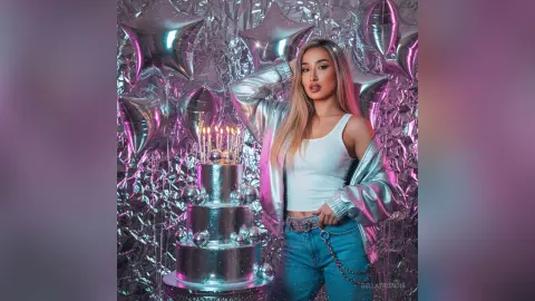 Glamorous woman in silver jacket and jeans celebrating with a silver birthday cake and star balloons.