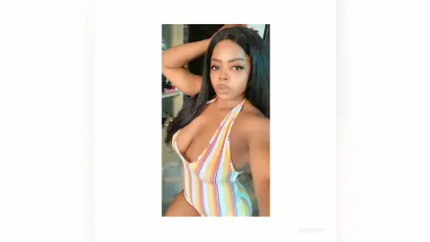 Young woman in a colorful striped one-piece swimsuit posing confidently in a bright indoor setting.
