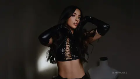 Moody portrait of a woman in a black lace-up corset and long leather gloves against a dark studio background.