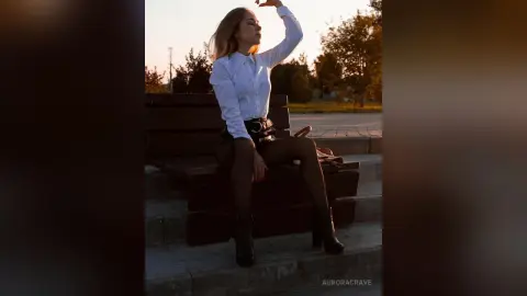 Blonde woman in a white button-down shirt and black skirt sitting on a park bench during a golden sunset.