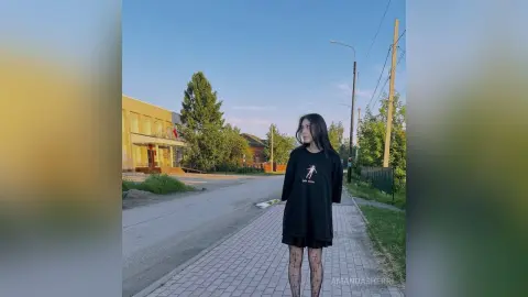 Young woman in a black graphic t-shirt and patterned tights standing on a city sidewalk under a clear blue sky.