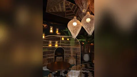 IrinaMolkova in a dimly lit room featuring large, white woven pendant lights and a matching wireframe booth or chairset over a dark table.