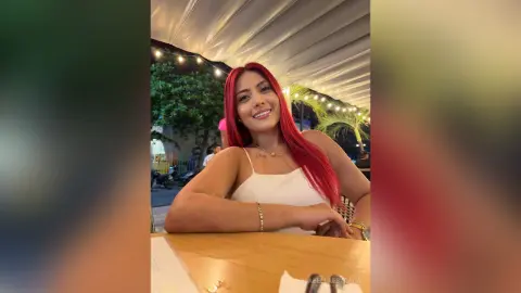 Smiling woman with bright red hair in a white tank top enjoying a night out at an outdoor restaurant.