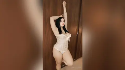 Curvy woman in a white lace corset bodysuit posing elegantly in a modern indoor setting.