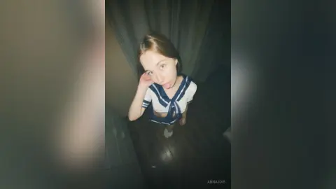 Young woman in a navy and white striped top posing playfully in a dimly lit room.