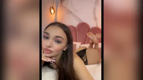 Young woman in black lace lingerie relaxing on a bed in a cozy, warm-lit bedroom.