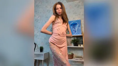 Young woman in a pink floral slip dress posing in a bright, modern room with aesthetic decor.
