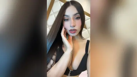 Young woman with long dark hair wearing a black sleeveless top in a soft, intimate indoor setting.